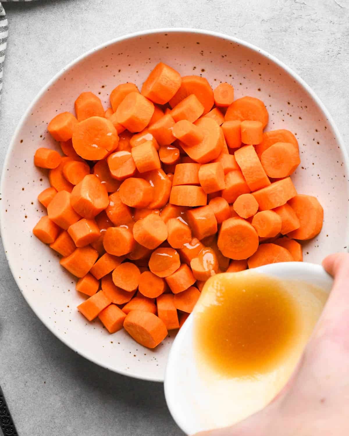 making glazed maple carrots - the maple and butter mixture being poured over carrots in a white bowl