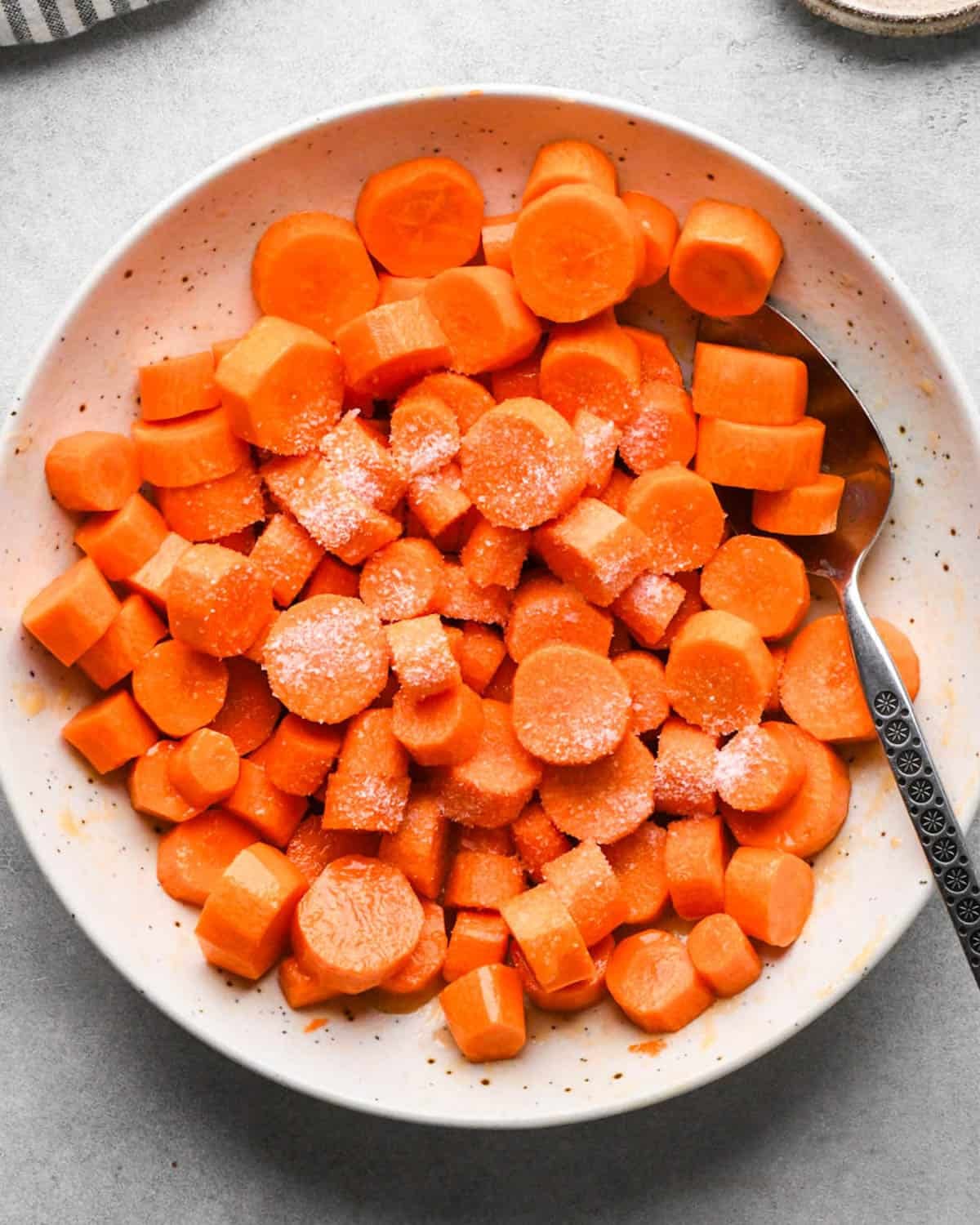 making glazed maple carrots - salt sprinkled on top of the chopped carrots in a white bowl with a silver spoon