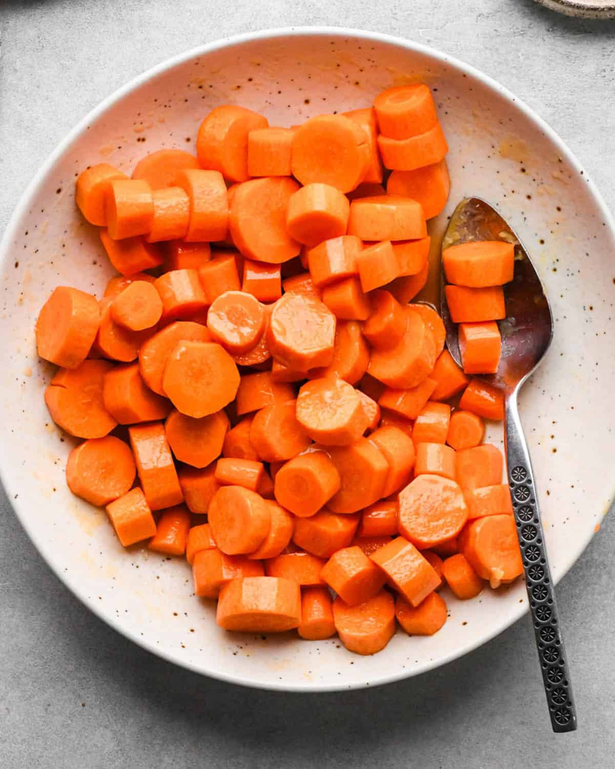 maple glazed carrots mixed together in a white bowl with a silver spoon
