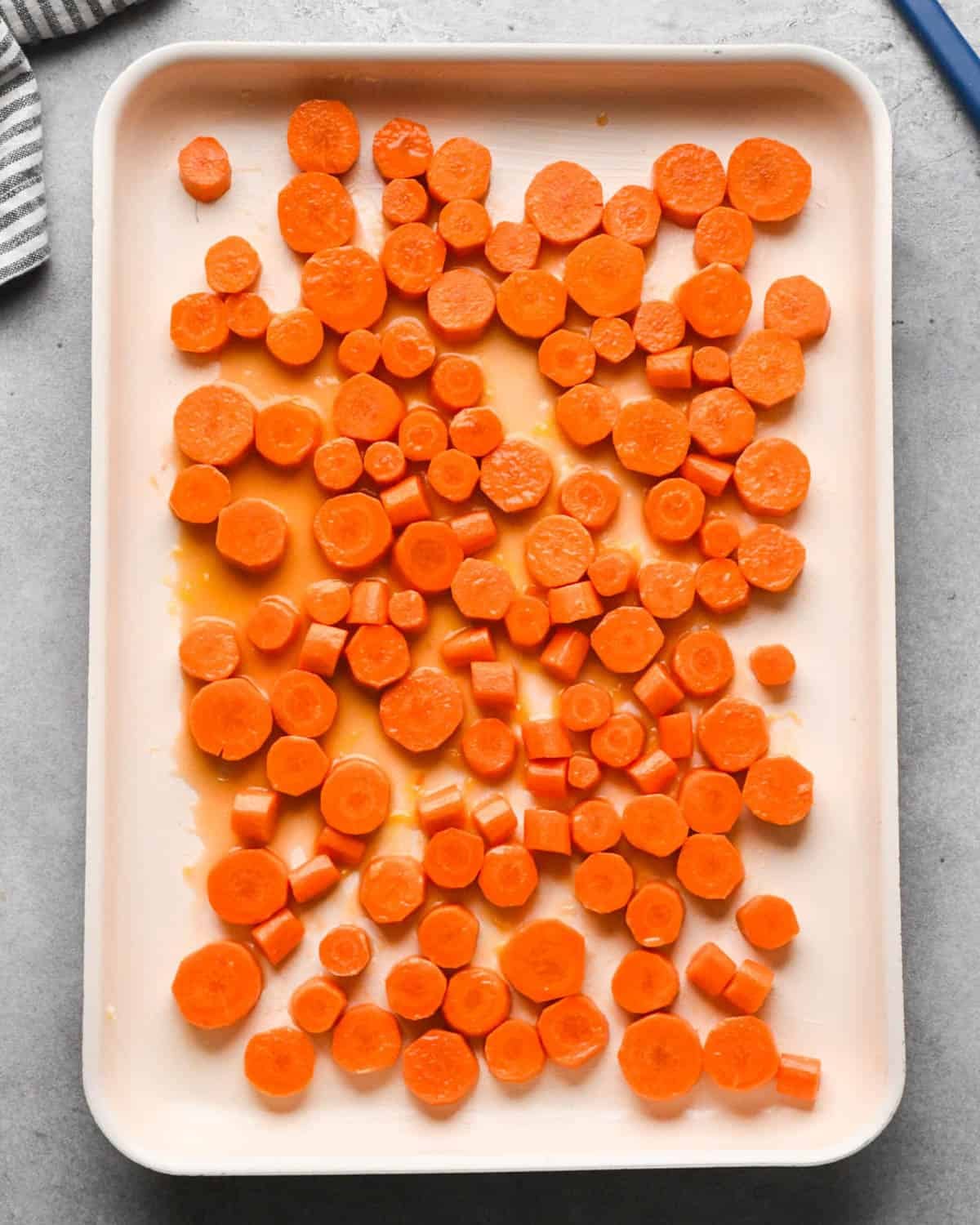 making glazed maple carrots - glaze and carrot mixture on a baking sheet spread into a single layer before baking
