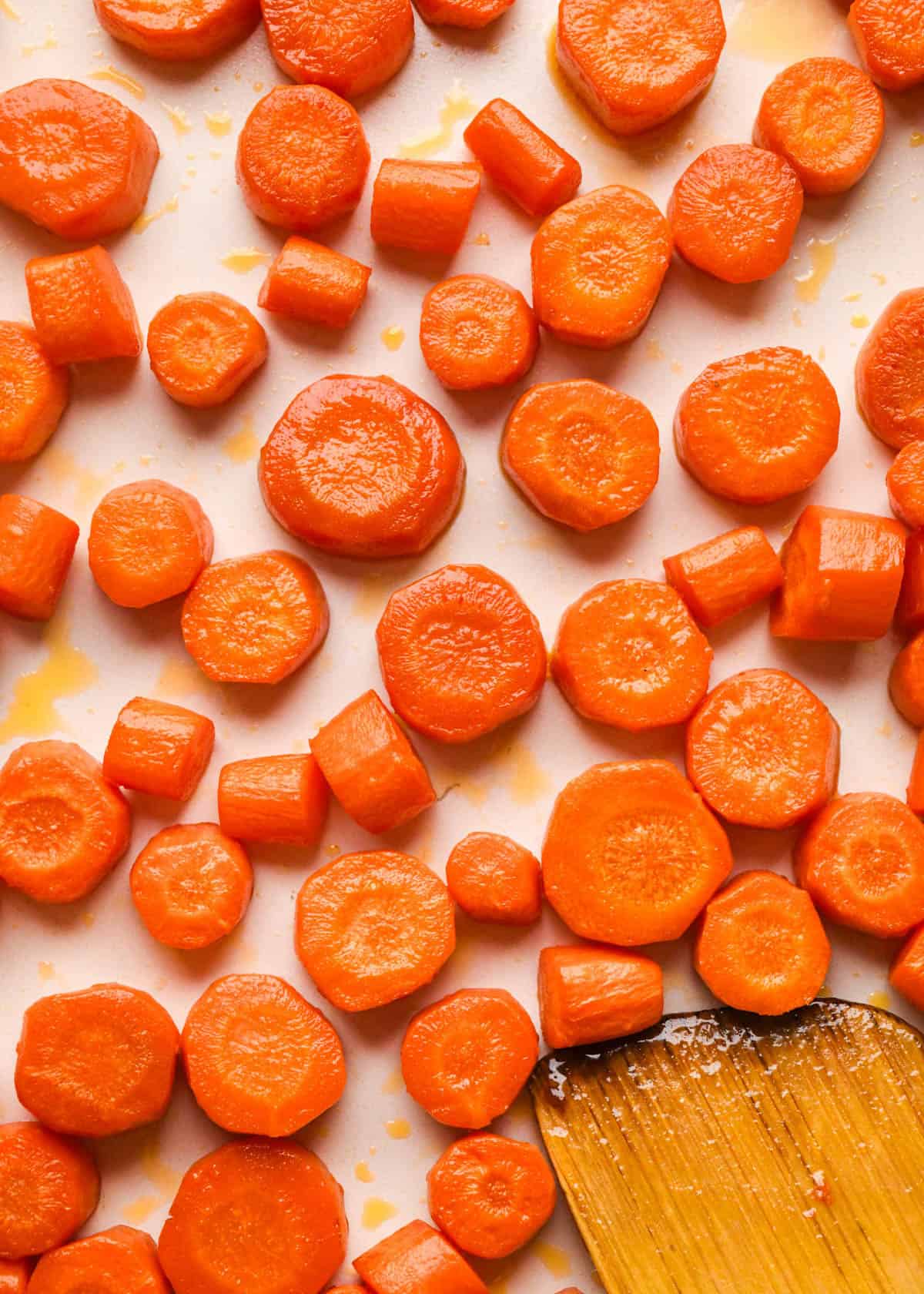 perfectly golden maple glazed carrots on a white baking sheet with a wooden spatula in the bottom left corner