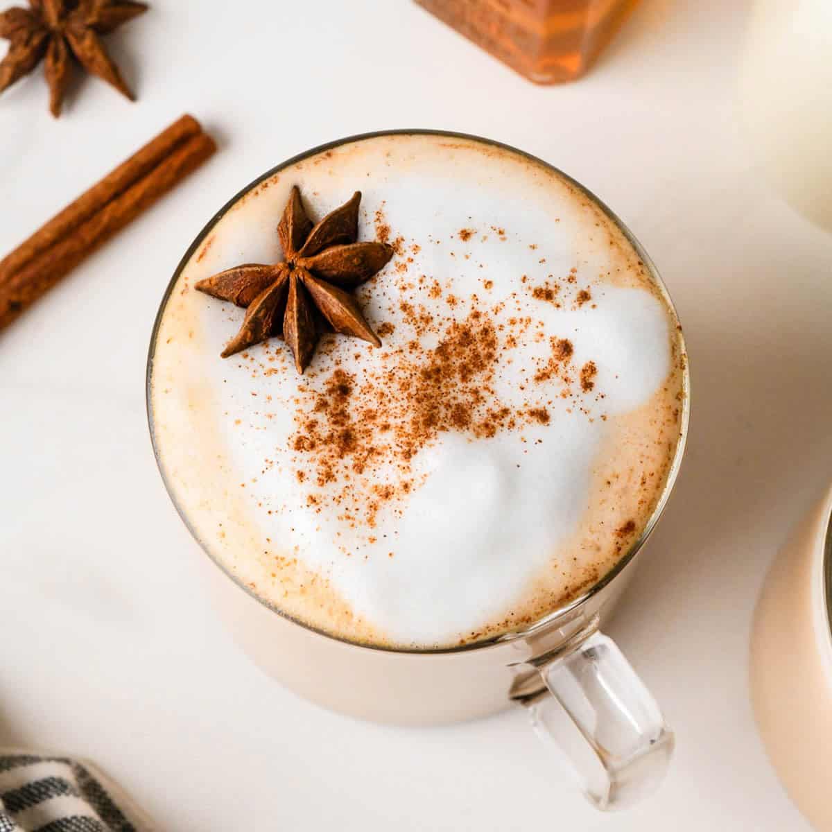 overhead photo of a chai latte in a glass mug topped with foamy milk, a sprinkle of cinnamon and star anise