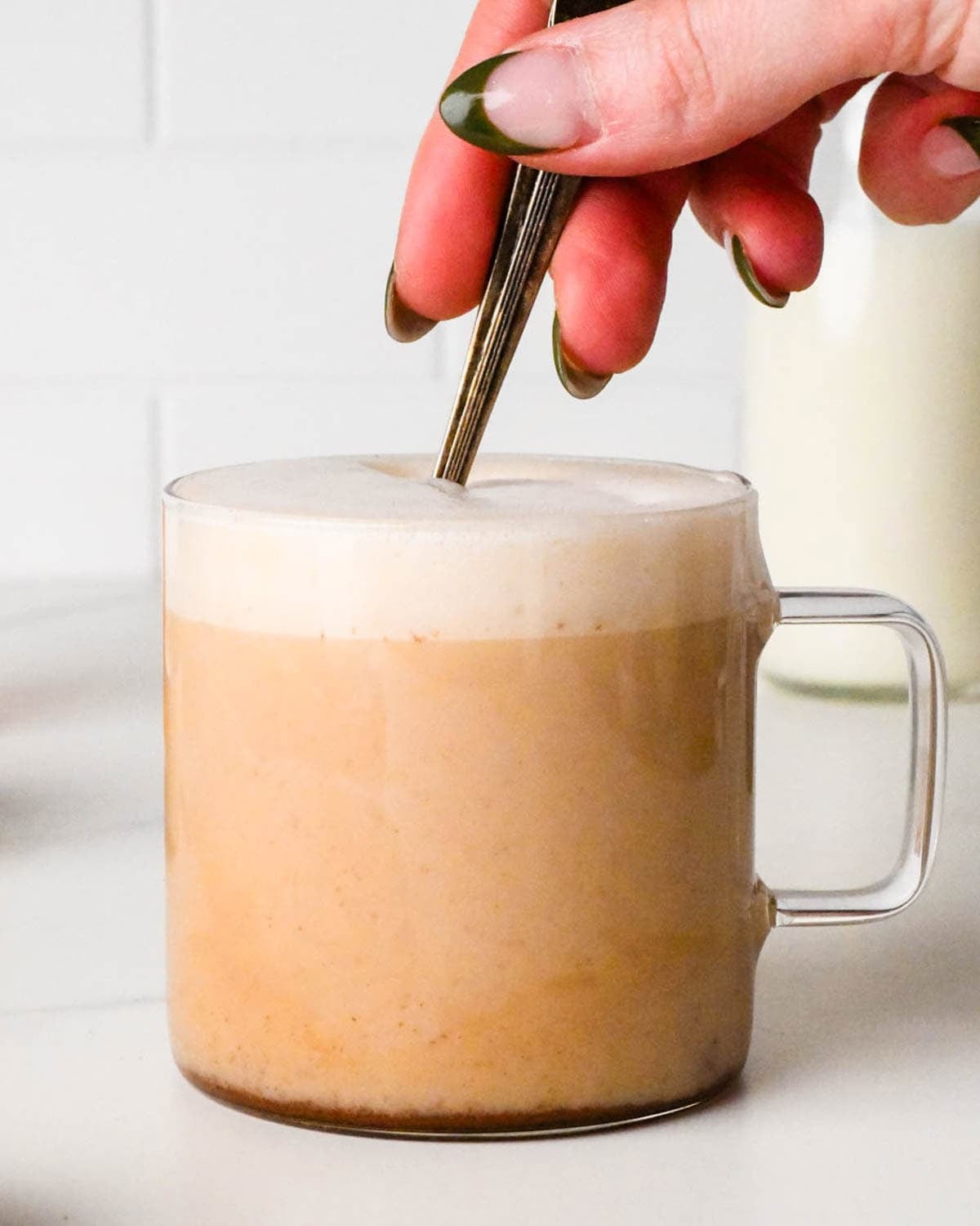 a hand stirring a chai tea latte in a glass mug