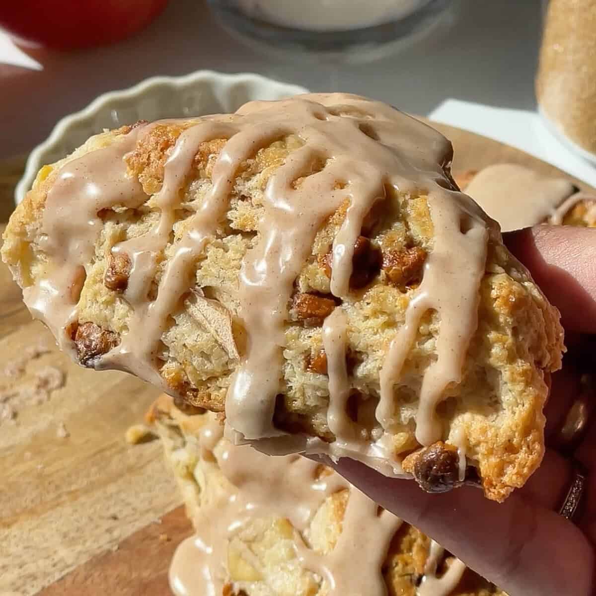 a hand holding a cinnamon apple scone with a cinnamon glaze and cinnamon chips in the scone.