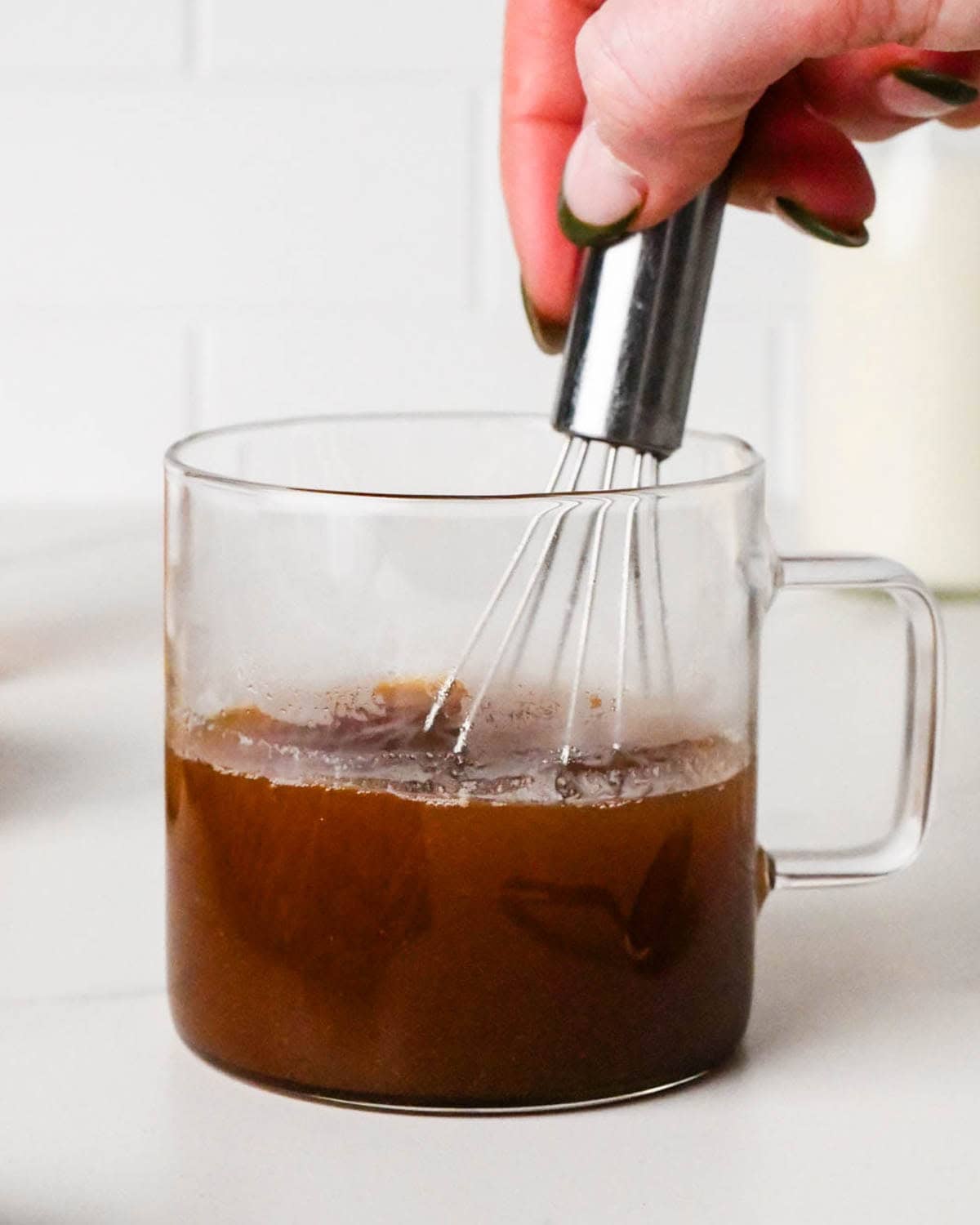 how to make a chai latte - a hand whisking the chai tea ingredients