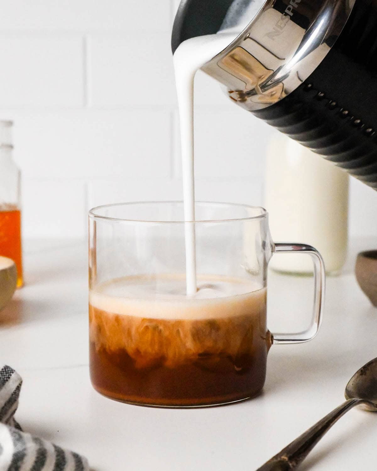 how to make a chai latte - frothed milk being poured into the tea in a glass mug