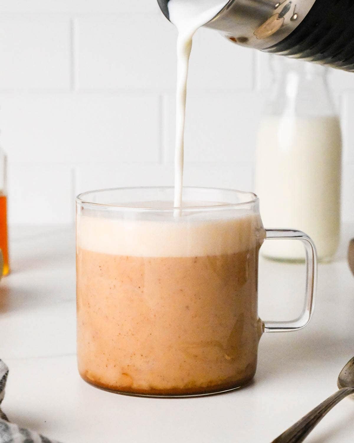 how to make a chai latte - frothed milk being poured into the tea in a glass mug