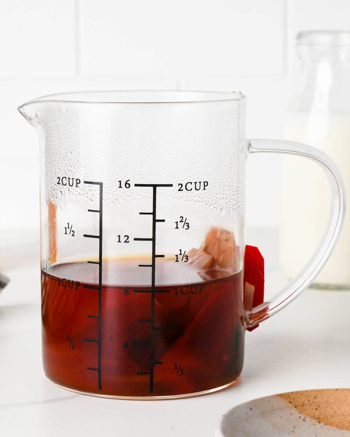 how to make a chai latte - front view of two chai tea bags brewing in a glass measuring cup