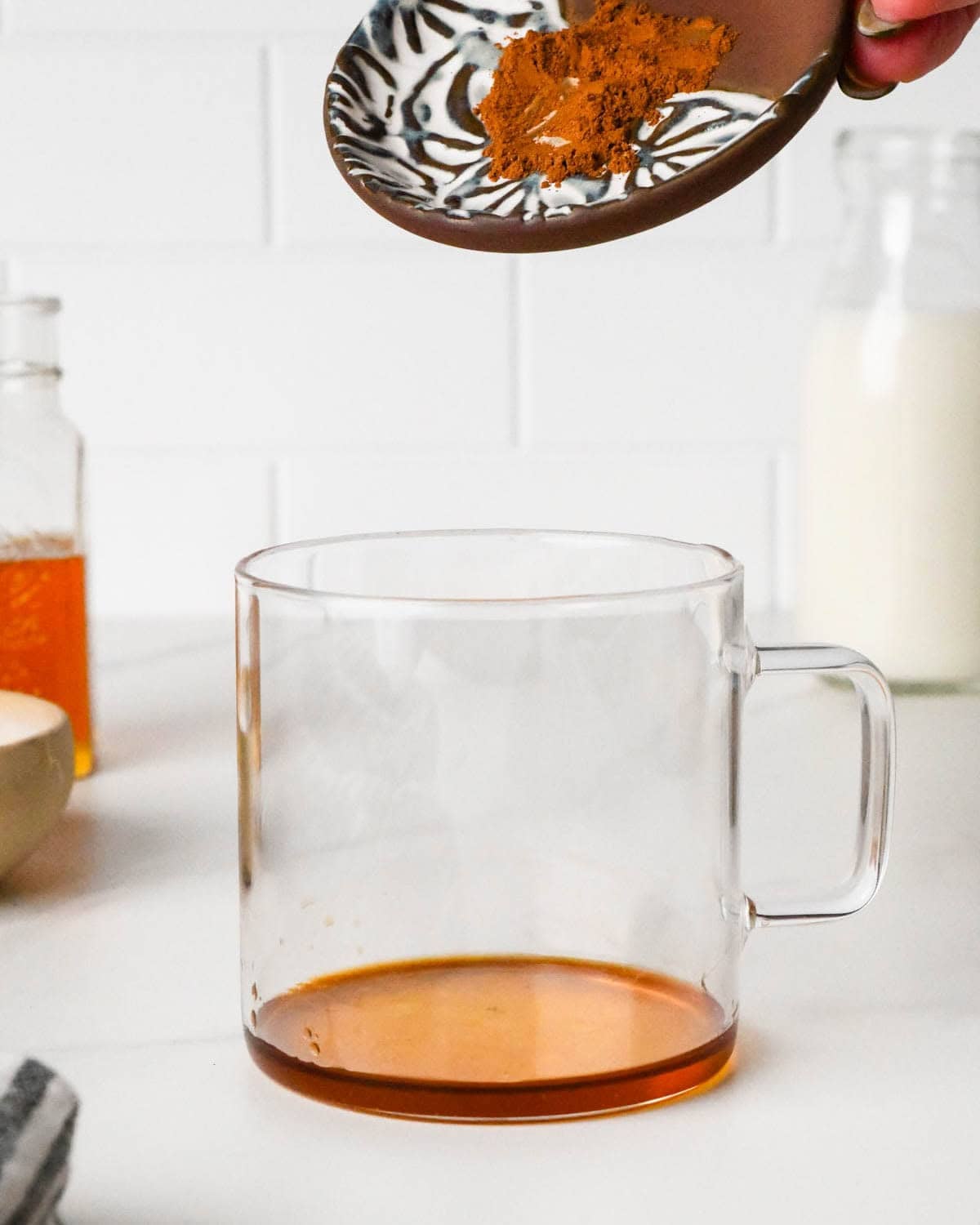 how to make a chai latte - a dish of ground cinnamon hovering over a glass mug