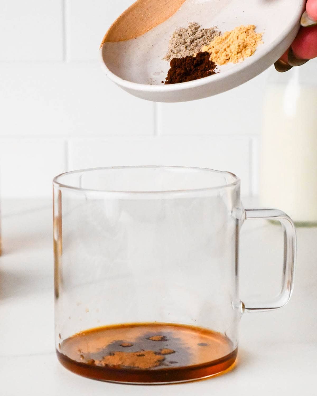 how to make a chai latte - a dish of ground cloves, ginger and cardamom hovering over a glass mug
