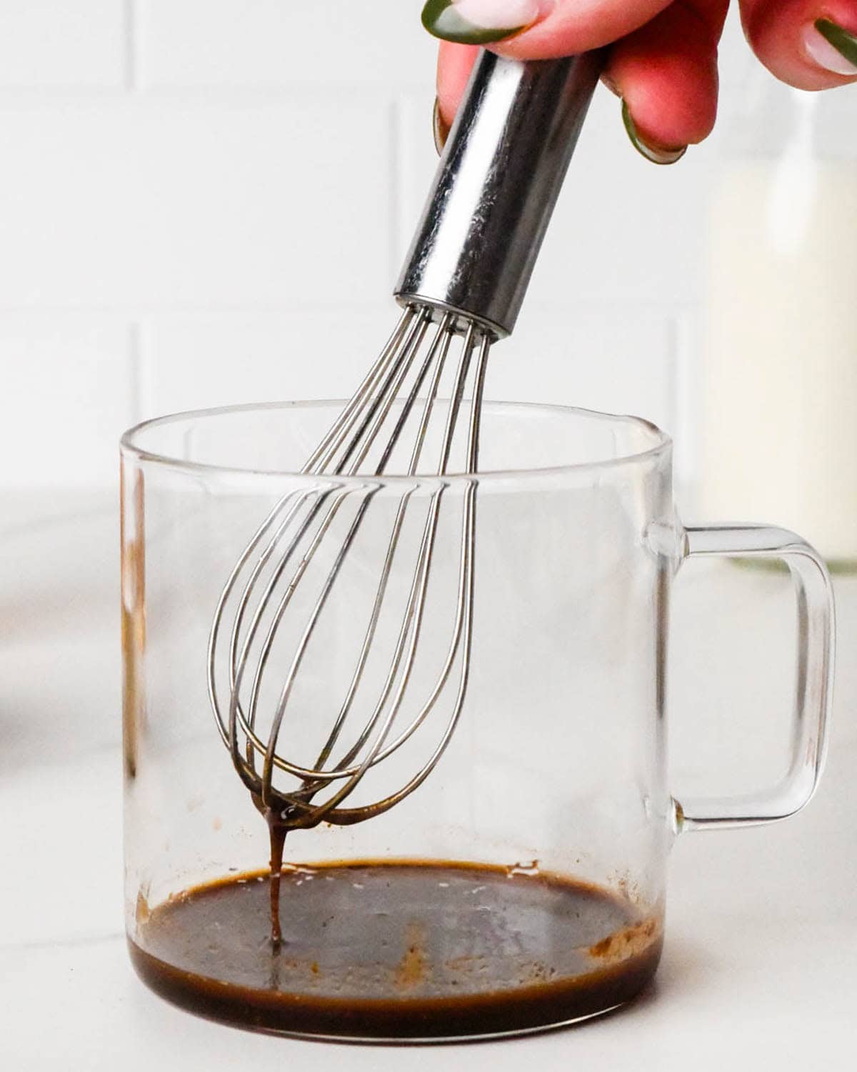how to make a chai latte - a hand whisking the ingredients in a glass mug