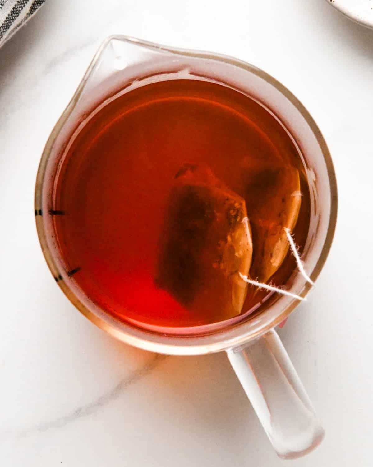 how to make a chai latte - overhead photo of two chai tea bags brewing in a glass measuring cup