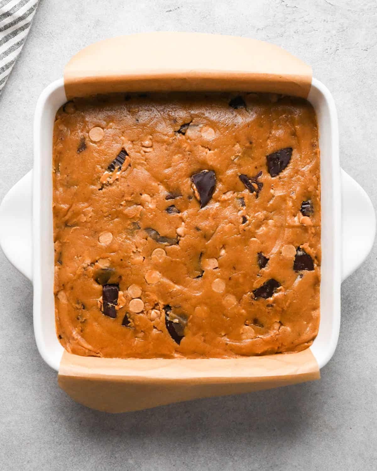 peanut butter blondies in a white ceramic baking dish lined with brown parchment paper before baking