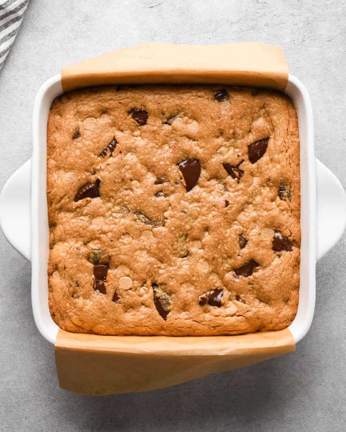 peanut butter blondies in a white ceramic baking dish lined with brown parchment paper after baking