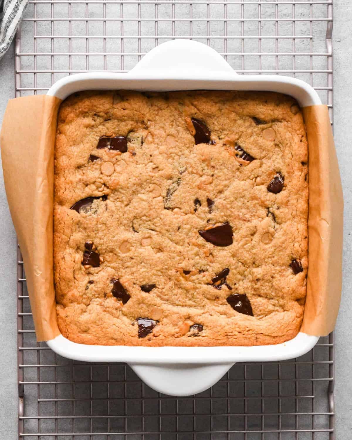 peanut butter blondies in a white ceramic baking dish lined with brown parchment paper after baking on a metal cooling rack
