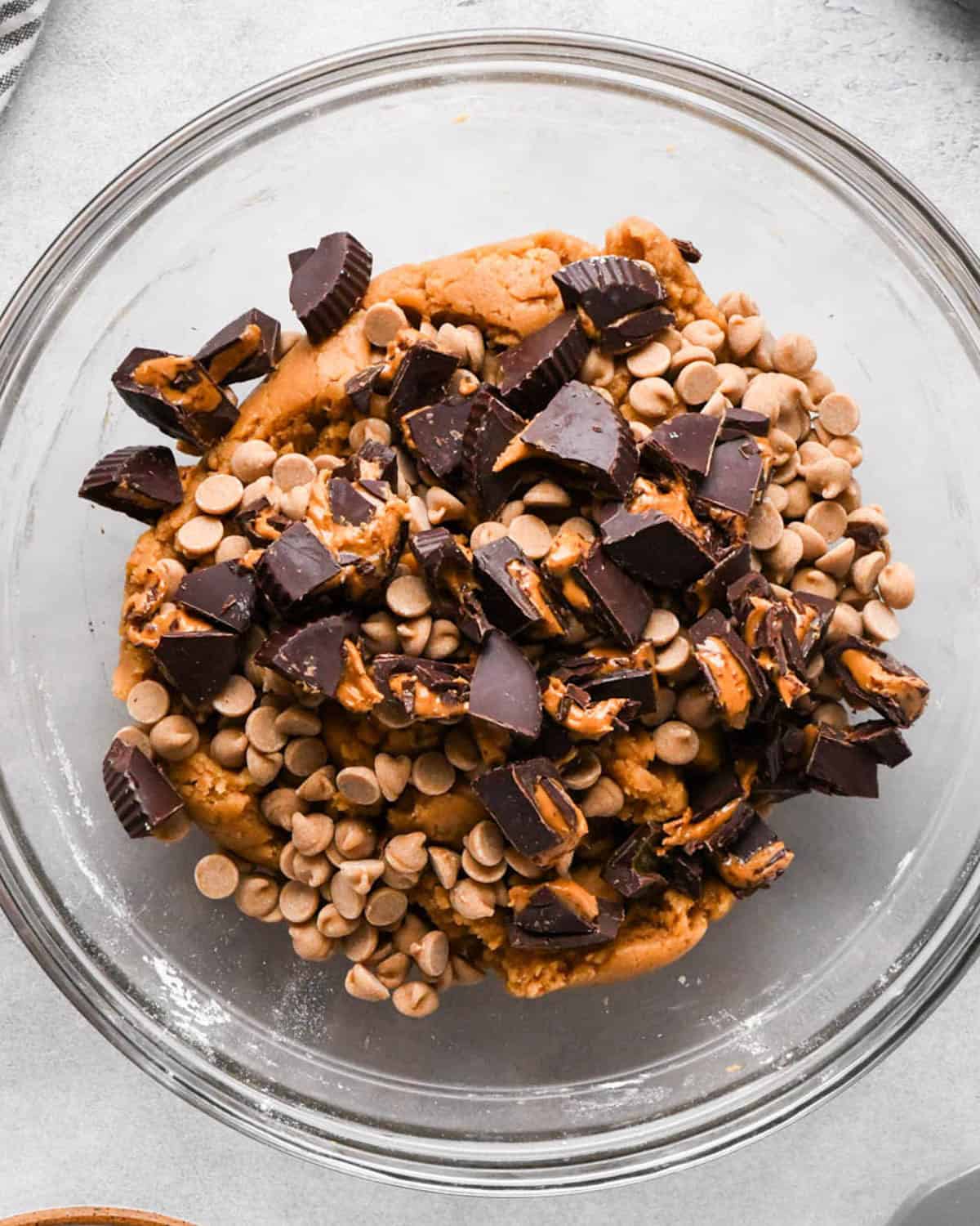 making peanut butter blondies - peanut butter chips and chopped peanut butter cups added to the dough before being mixed in, in a glass bowl