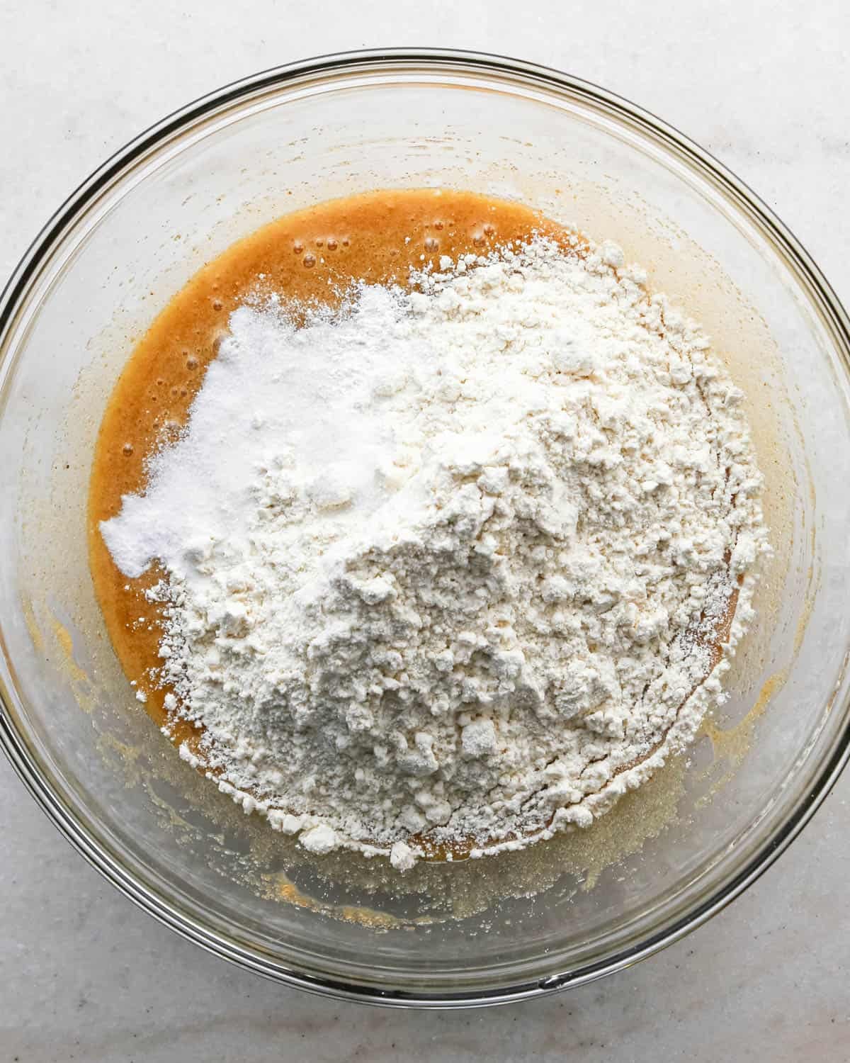 making brown butter cookie bars - dry ingredients added to the wet ingredients in a glass mixing bowl before mixing together