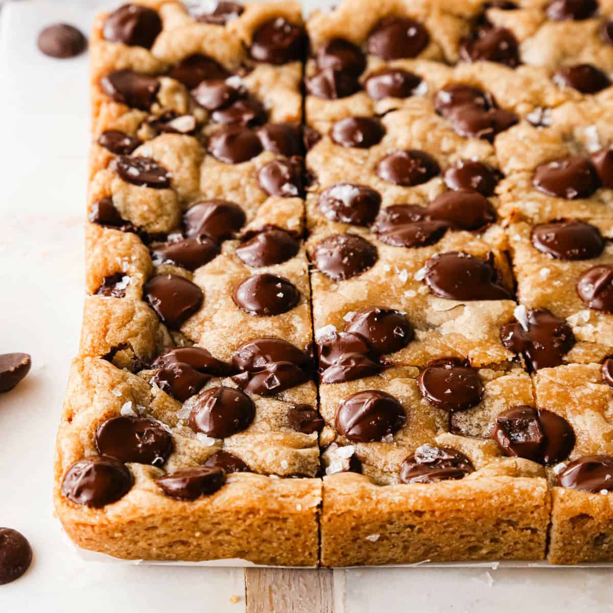 front view of brown butter cookie bars on a marble cutting board cut into 16 squares with melty chocolate chips and topped with flaky sea salt.