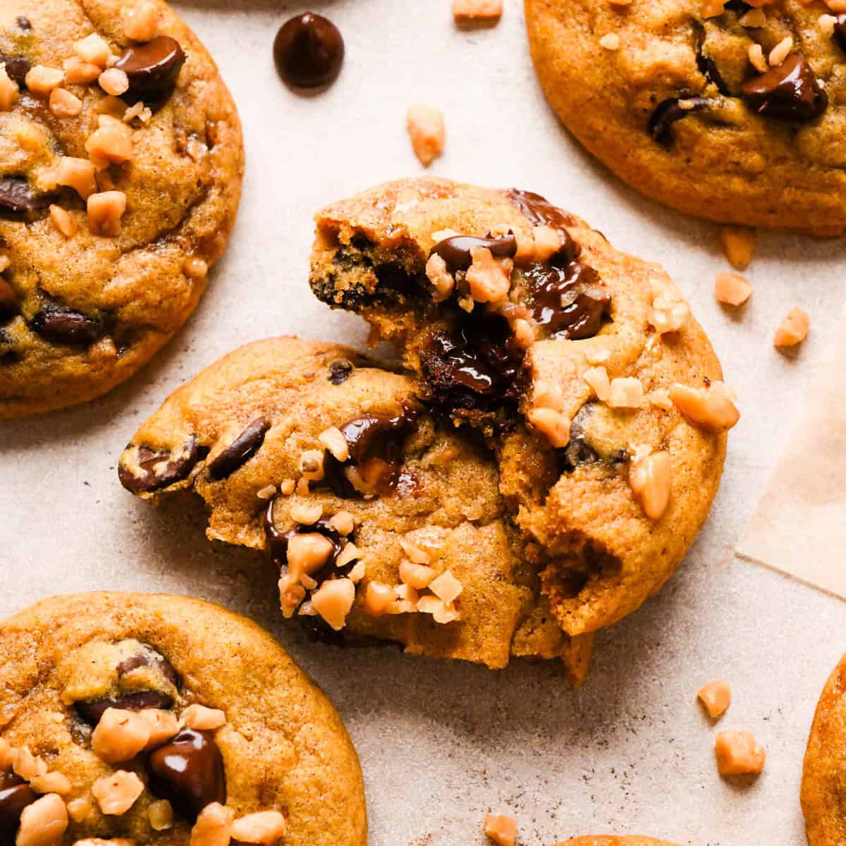 4 brown butter pumpkin cookies, one is cut in half with the two halves resting on each other so you can see the melty chocolate chips inside.