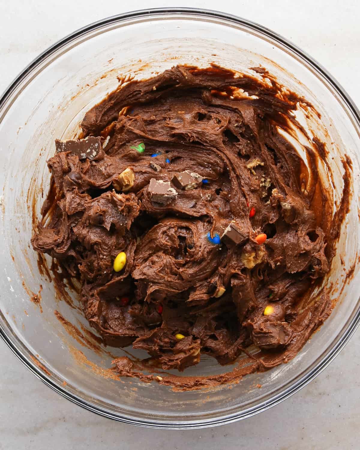 making candy halloween brownies - final brownie batter in a glass mixing bowl with chopped candy. mixed into the batter
