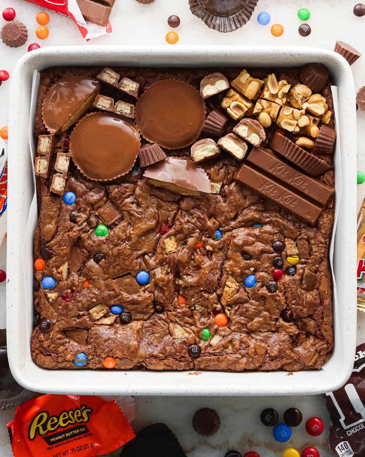 candy being added to the top of the baked halloween brownies in a white ceramic baking dish with candy surrounding it