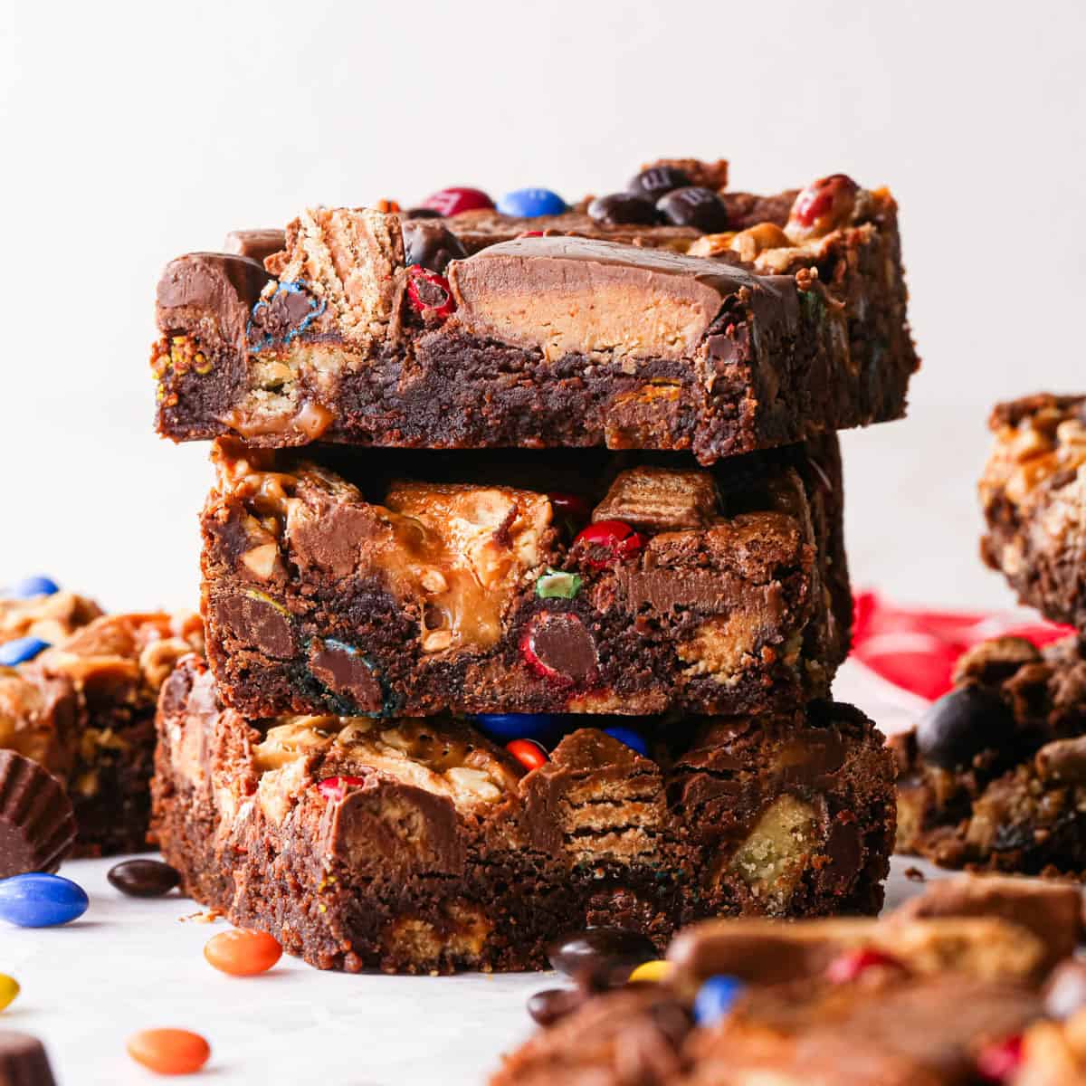 a stack of 3 leftover candy halloween brownies with the fudgy texture and candy mixed in clearly visible, surrounded by more brownies and candy