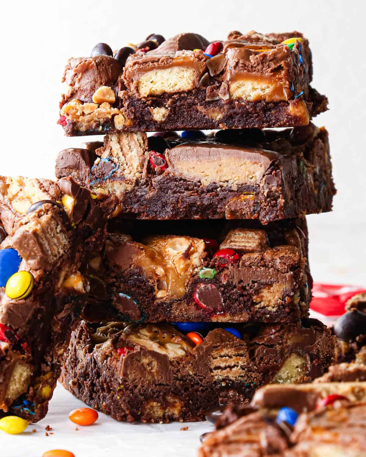 a stack of 4 leftover candy halloween brownies with the fudgy texture and candy mixed in clearly visible, surrounded by more brownies and candy