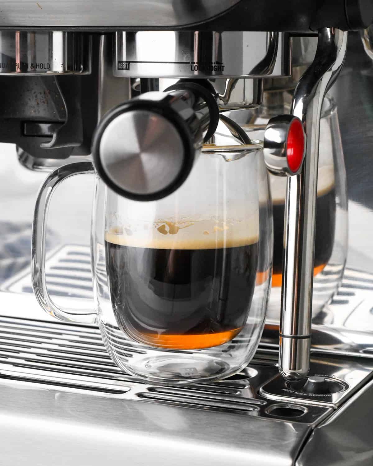 how to make a vanilla latte - espresso brewed into the glass mug which is on an espresso machine
