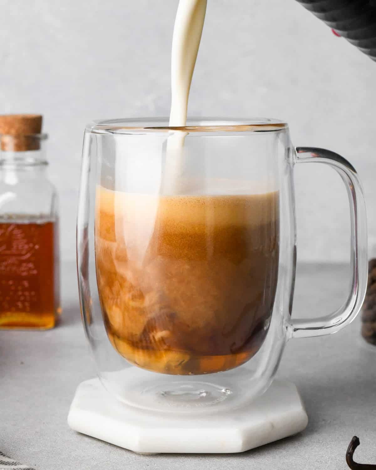 how to make a vanilla latte - front view of frothed milk being poured into the glass mug with espresso and honey