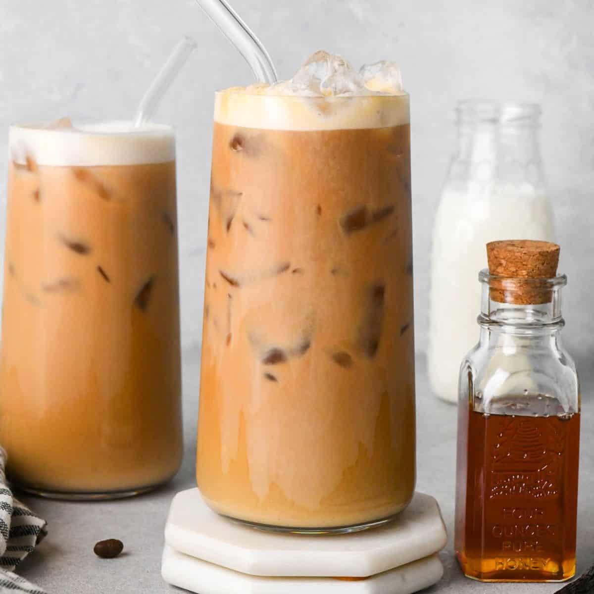 two iced vanilla latte in glass with glass straws. surrounded by a jar of honey and milk