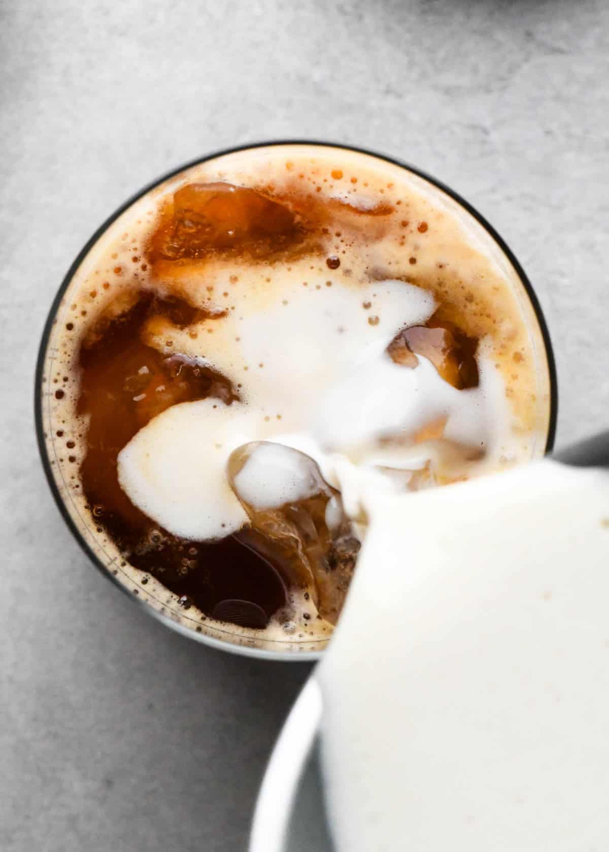how to make an iced vanilla latte - overhead photo of frothed milk being poured into a glass of ice and brewed espresso