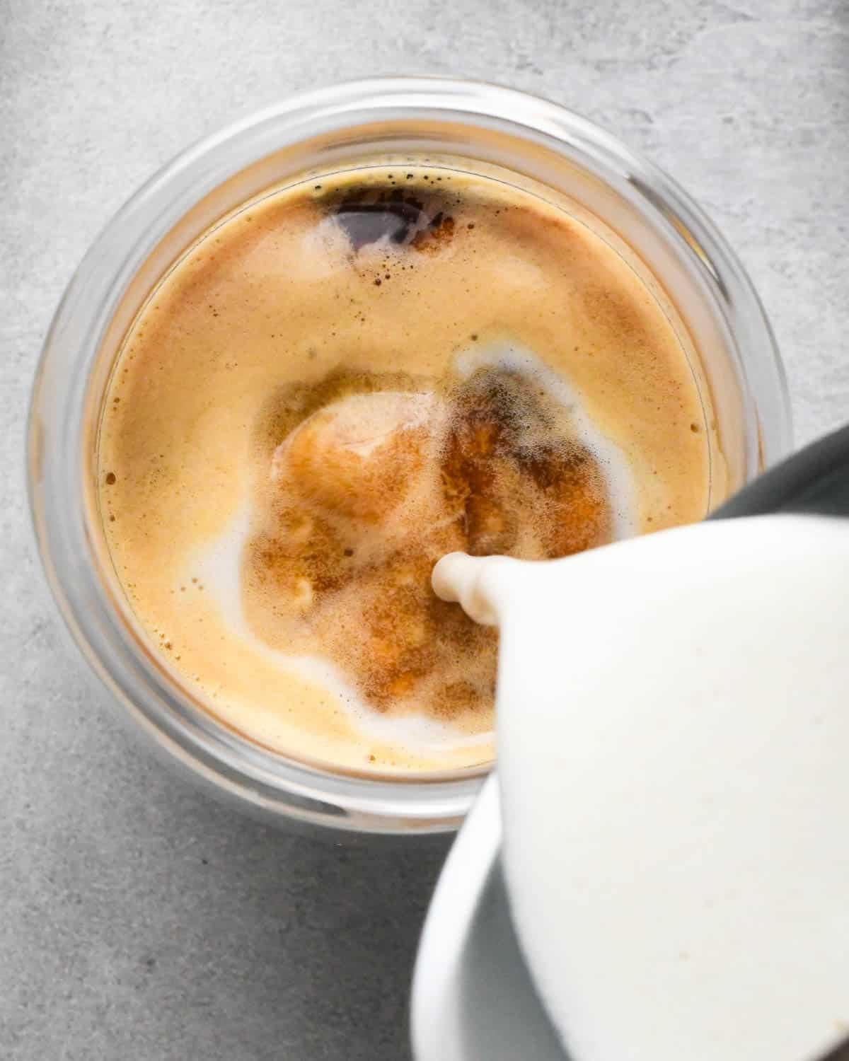 how to make a vanilla latte - overhead view of frothed milk being poured into the glass mug with espresso and honey