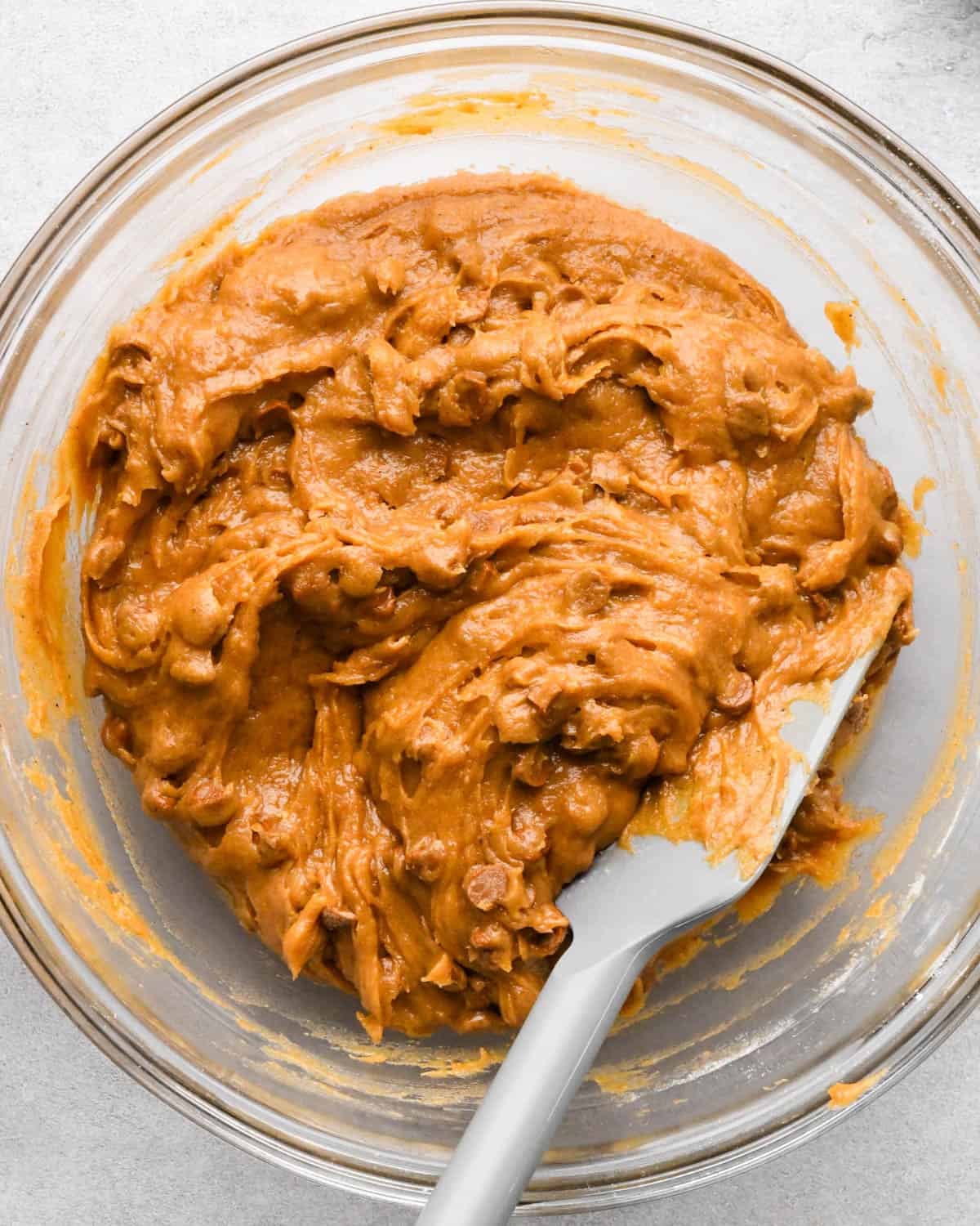 making pumpkin blondies - final batter with cinnamon chips mixed in, in a glass bowl with a gray spatula