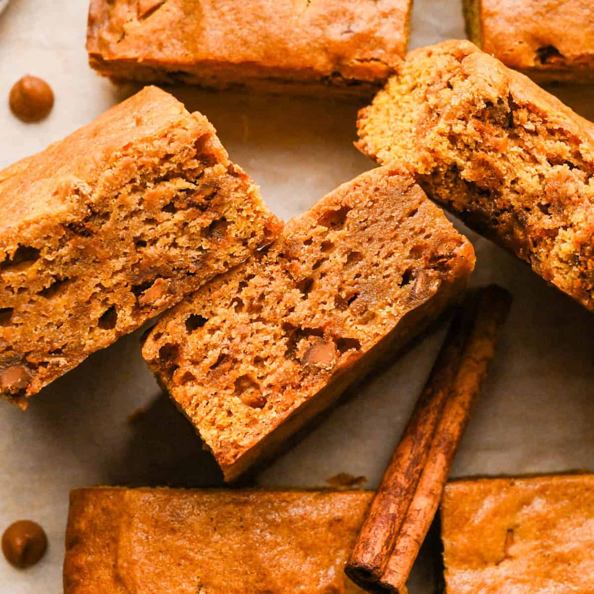 3 pumpkin blondies with cinnamon chips on their side so the chewy texture is showing on parchment paper surrounded by more pumpkin blondies and cinnamon chips