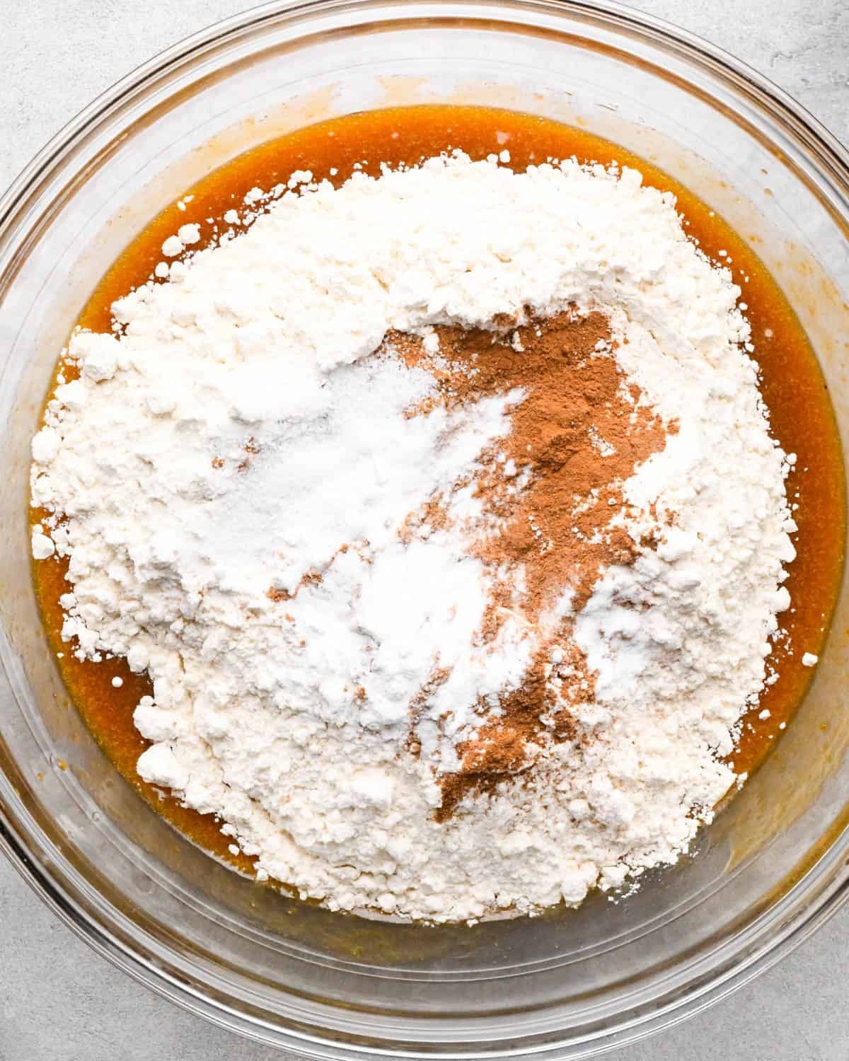 making pumpkin blondies - flour, baking soda, baking powder, cinnamon, salt and pumpkin pie spice added to the wet mixture in a glass bowl before mixing