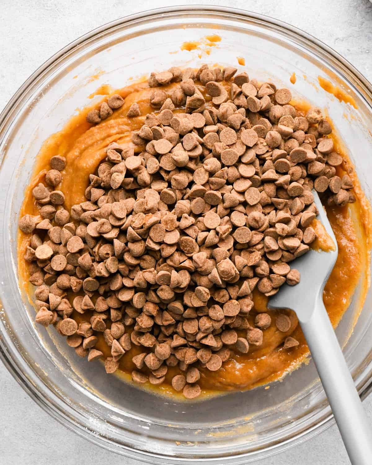 making pumpkin blondies - cinnamon chips added to the batter in a glass mixing bowl with a gray spatula before mixing