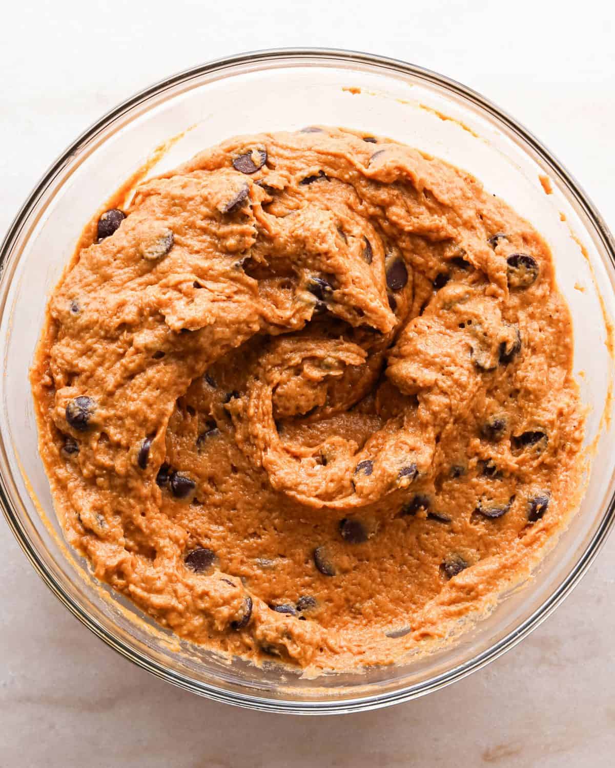 Making pumpkin chocolate chip bars: overhead photo of chocolate chips being added to the batter in a clear mixing bowl and mixed together.