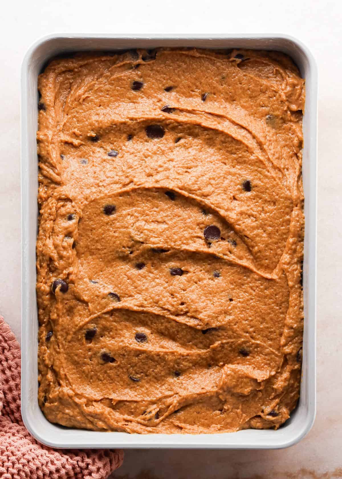 Making pumpkin chocolate chip bars: overhead photo of batter spread out in a greased silver baking dish and ready to bake.