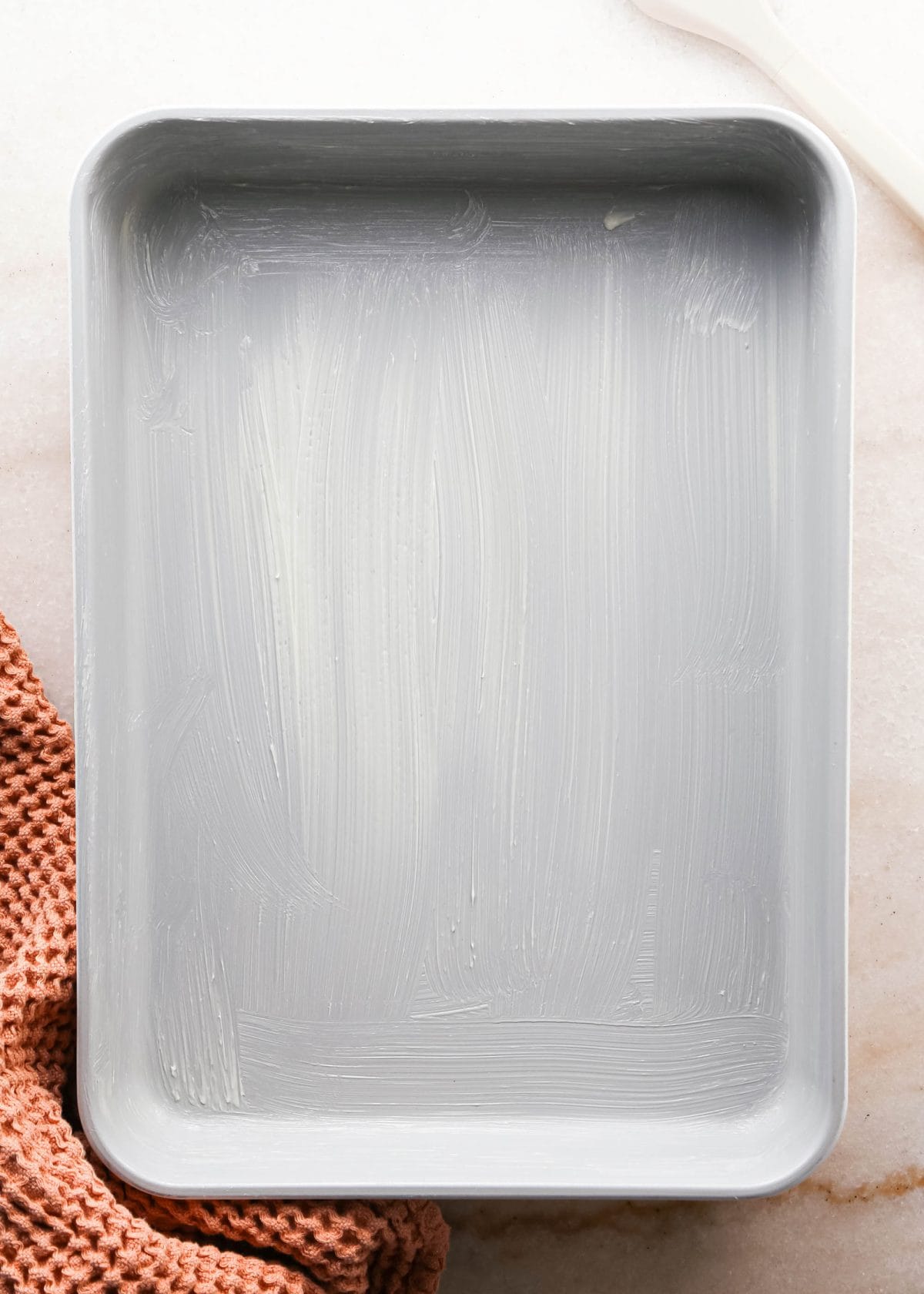 Making pumpkin chocolate chip bars: overhead photo of a silver baking dish coated with butter and sitting on a light countertop with a towel nearby.