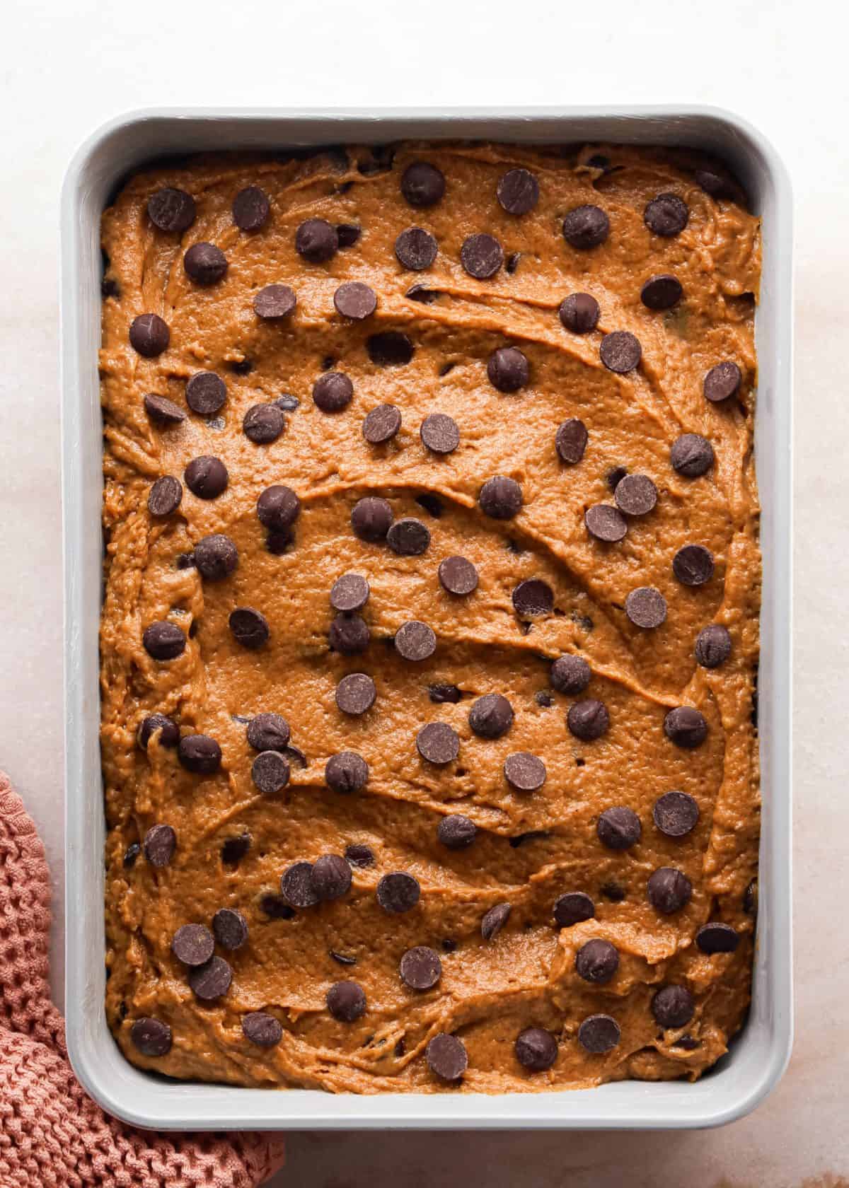 Making pumpkin chocolate chip bars: overhead photo of batter spread out in a greased silver baking dish, topped with additional chocolate chips, and ready to bake.