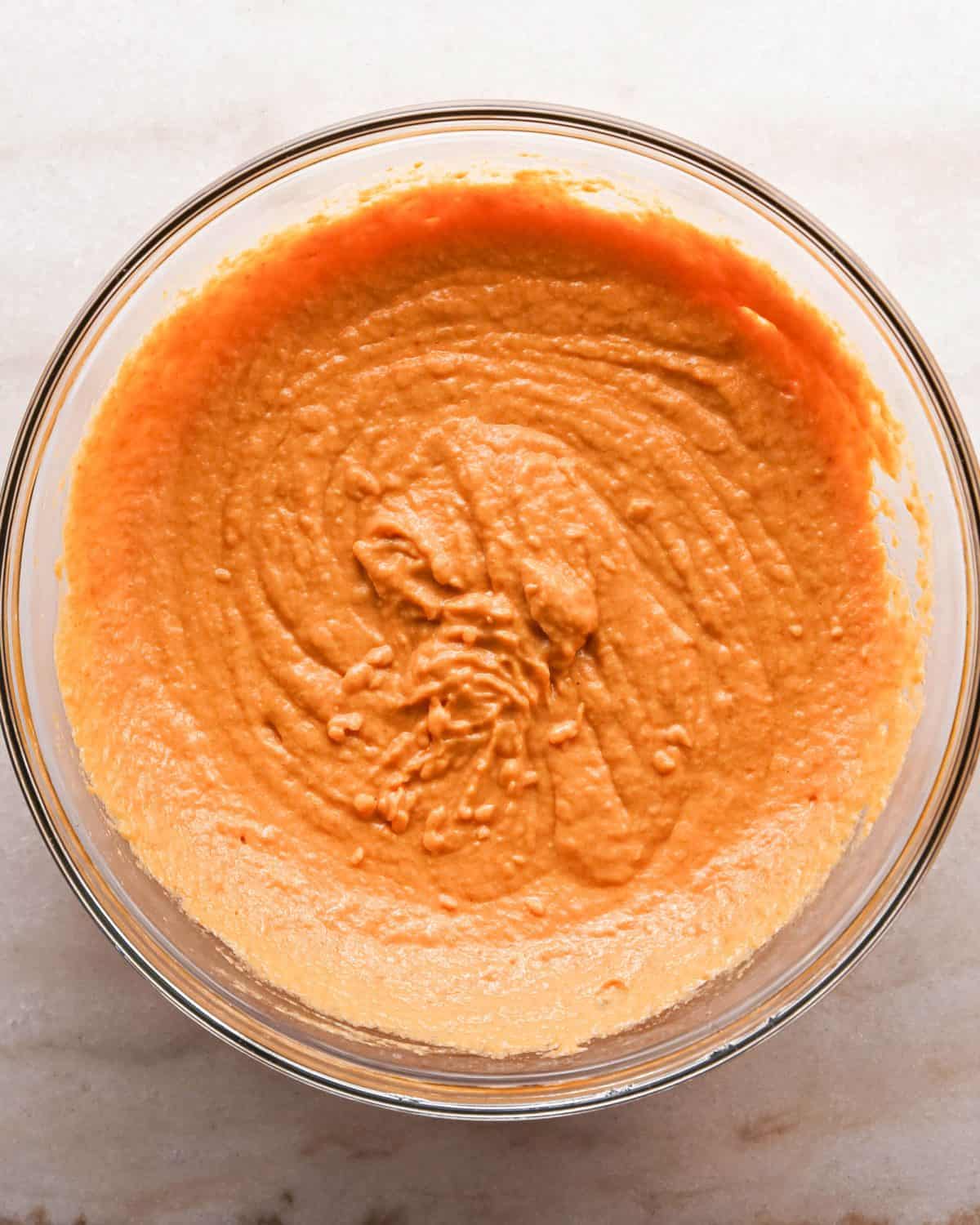 Making pumpkin chocolate chip bars: overhead photo of a clear mixing bowl with pumpkin, butter, sour cream, whole milk, eggs, and vanilla mixed together.