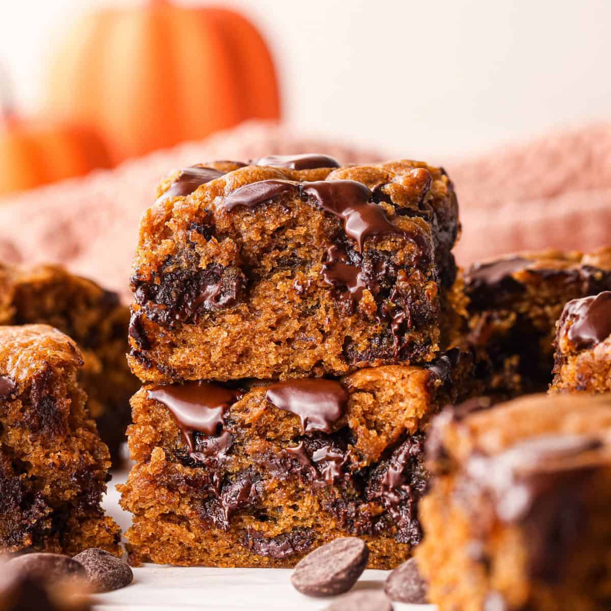 Close-up of homemade pumpkin chocolate chip bars with a moist, soft pumpkin-spice crumb, generously packed with melty chocolate chips and chunks, stacked together and topped with melted chocolate for a rich, cozy fall dessert.