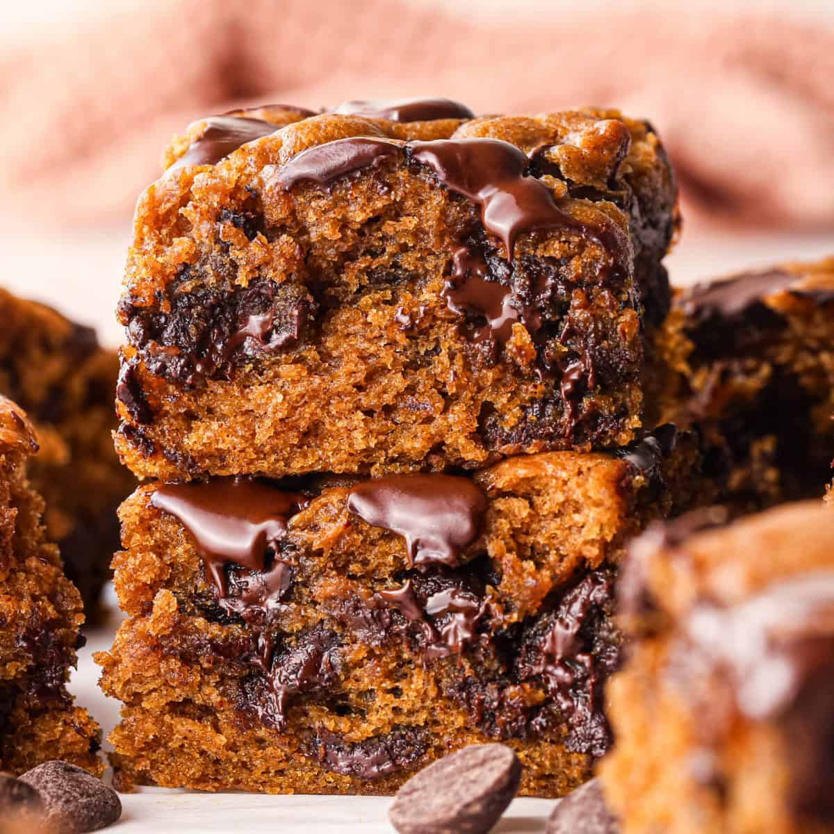 Close-up of homemade pumpkin chocolate chip bars with a moist, soft pumpkin-spice crumb, generously packed with melty chocolate chips and chunks, stacked together and topped with melted chocolate for a rich, cozy fall dessert.
