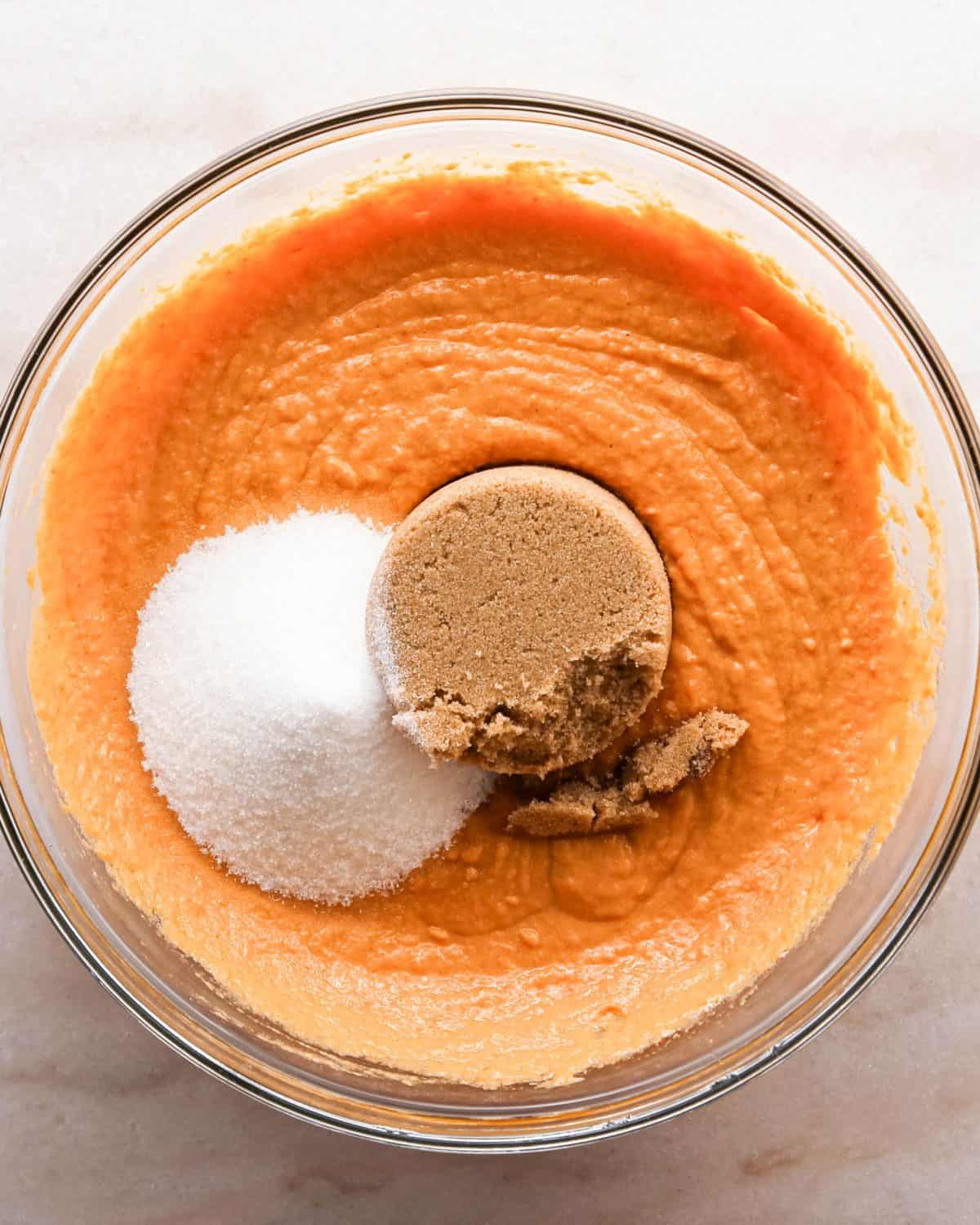 Making pumpkin chocolate chip bars: overhead photo of a clear mixing bowl with sugar and brown sugar added to the wet ingredients mixture.