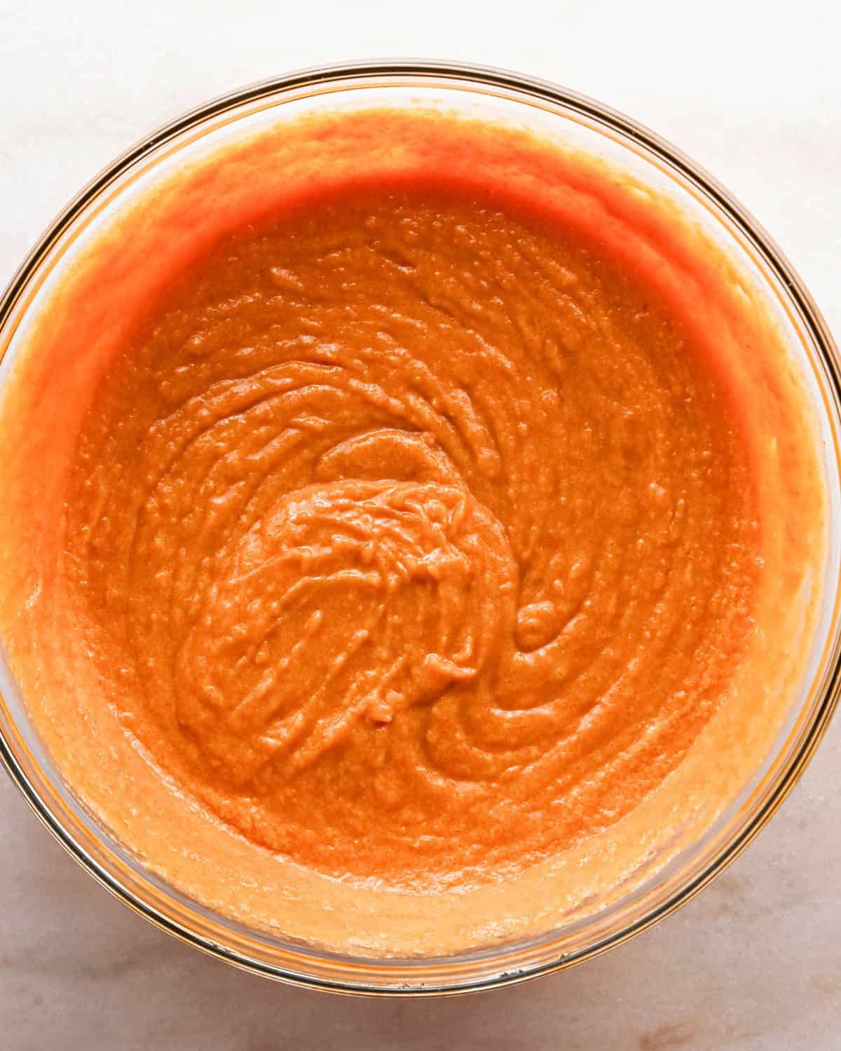 Making pumpkin chocolate chip bars: overhead photo of a clear mixing bowl with sugar and brown sugar added to the wet ingredients mixture and mixed together.