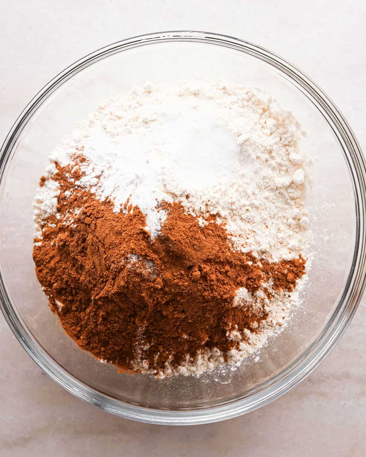 Making pumpkin chocolate chip bars: overhead photo of a clear mixing bowl with flour, baking soda, baking powder, sea salt, cinnamon, and pumpkin pie spice put together.