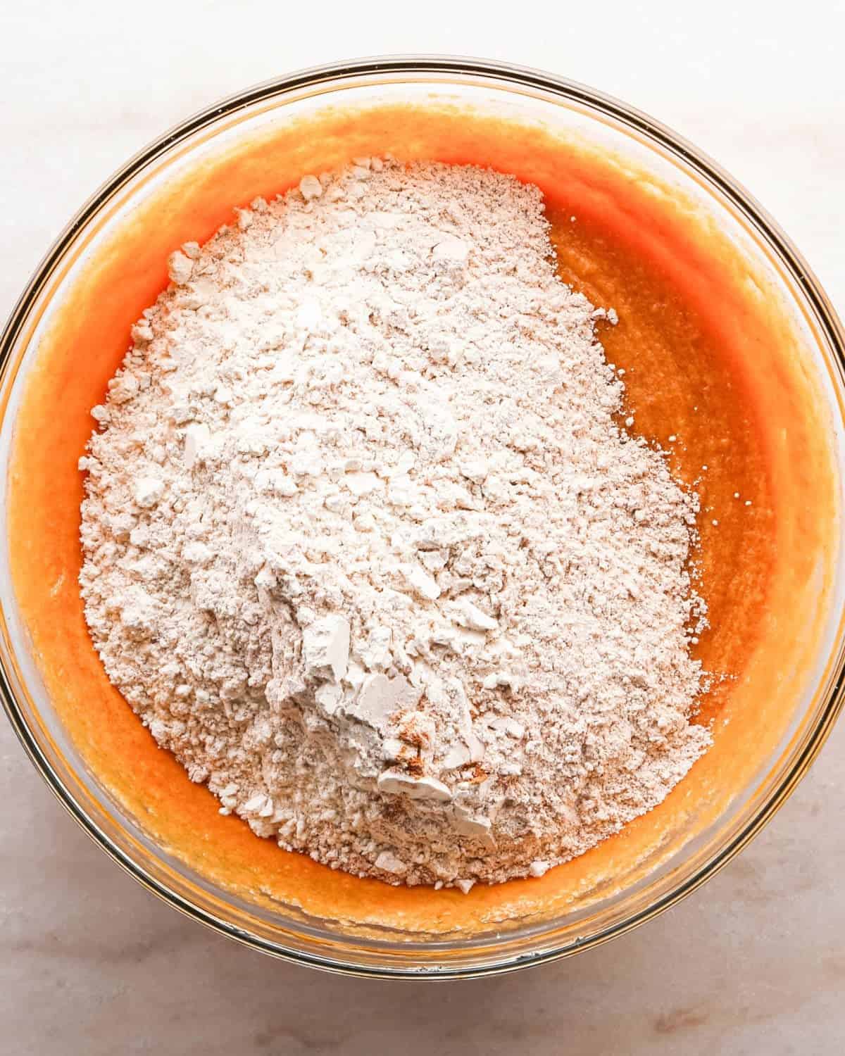 Making pumpkin chocolate chip bars: overhead photo of dry ingredients added to the wet ingredients in a clear mixing bowl.