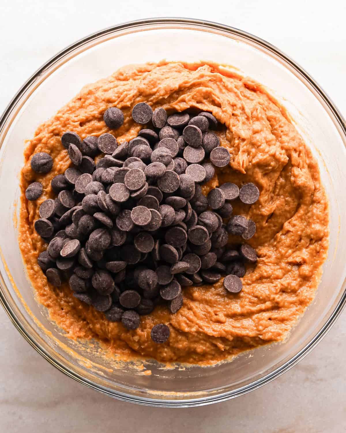 Making pumpkin chocolate chip bars: overhead photo of chocolate chips being added to the batter in a clear mixing bowl.