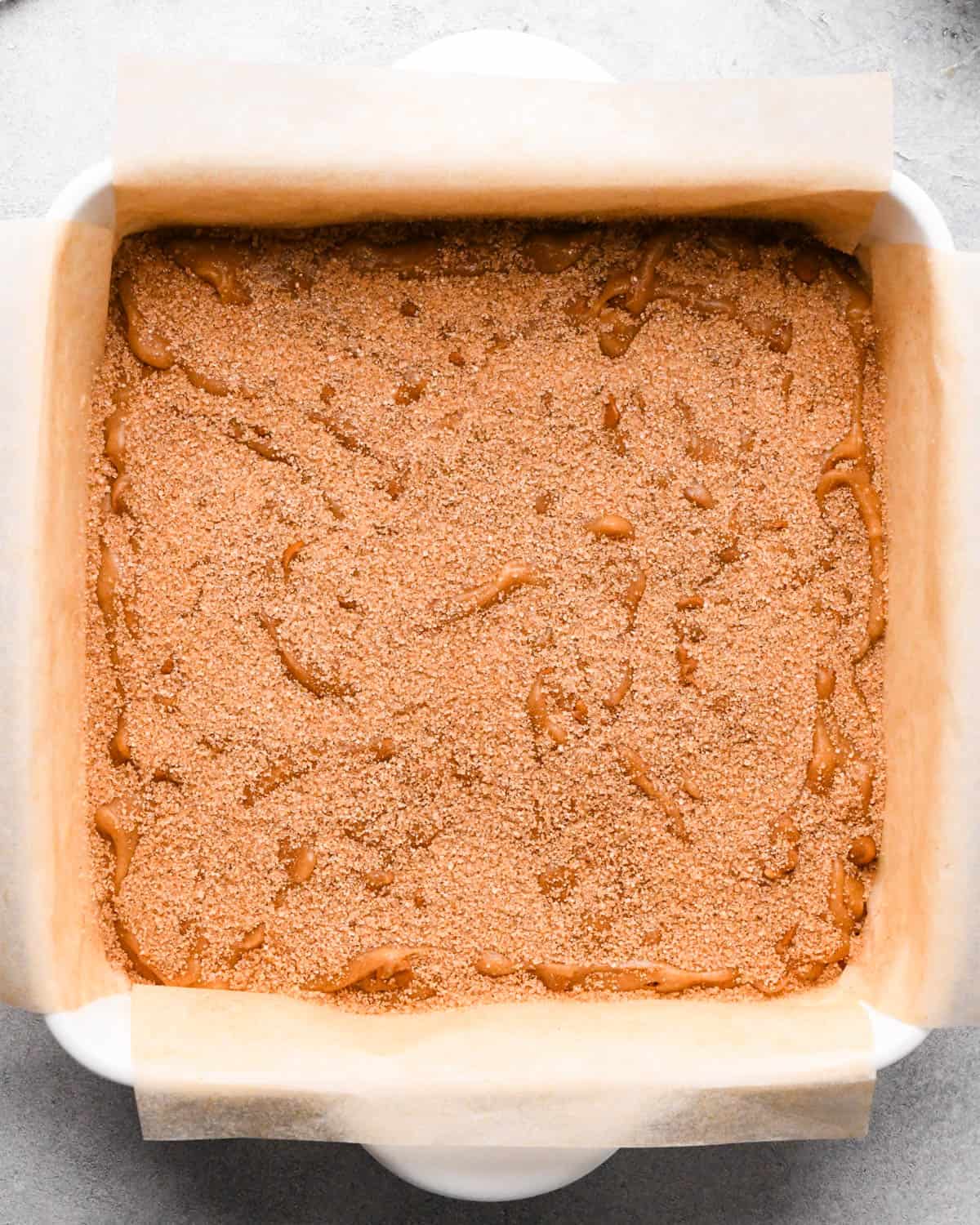 making snickerdoodle blondies -cinnamon sugar spread onto the unbaked snickerdoodle blondies in a white, parchment-lined baking dish
