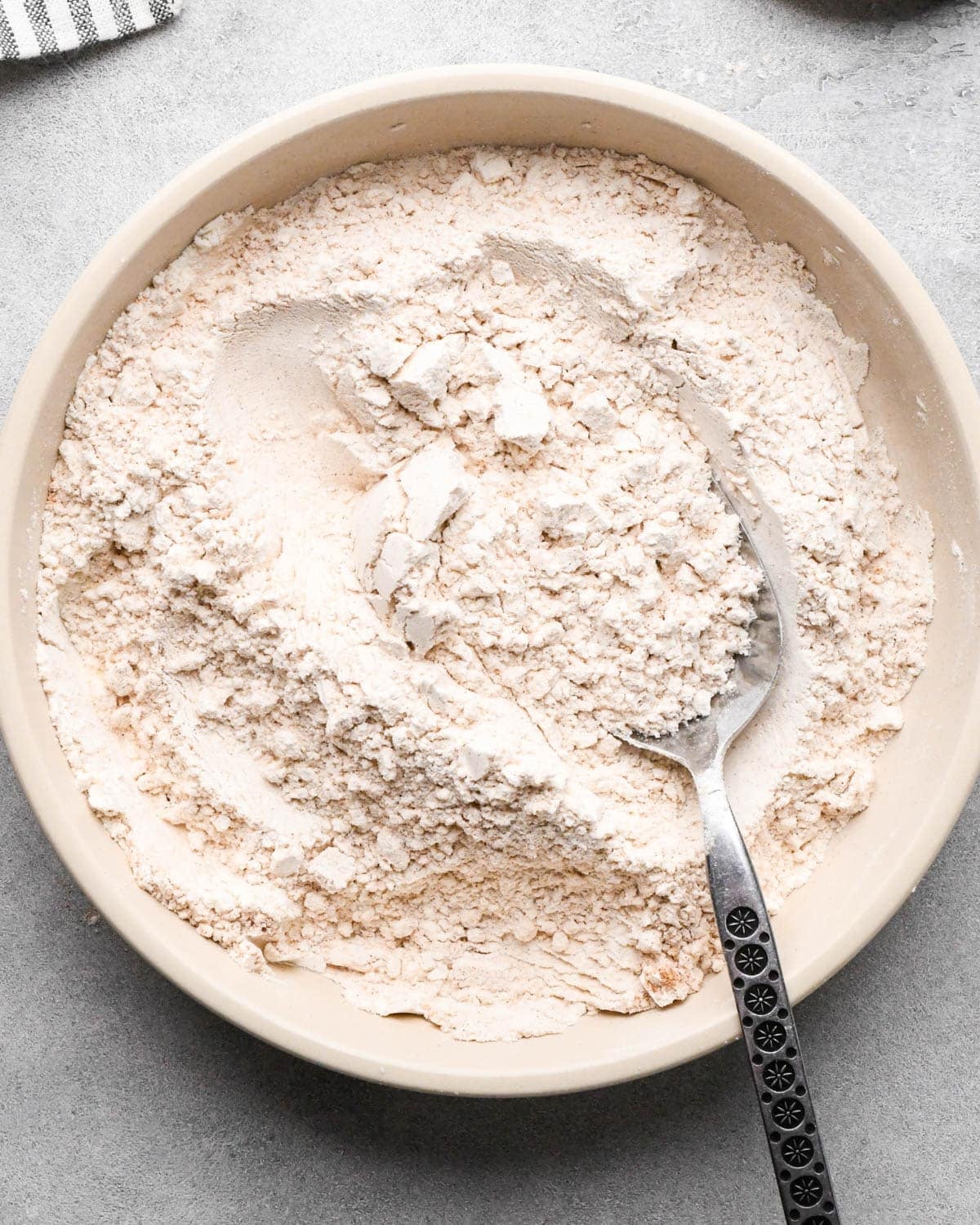 making snickerdoodle blondies -flour, cream of tartar, baking soda, cinnamon and salt in a white bowl with a silver spoon after mixing